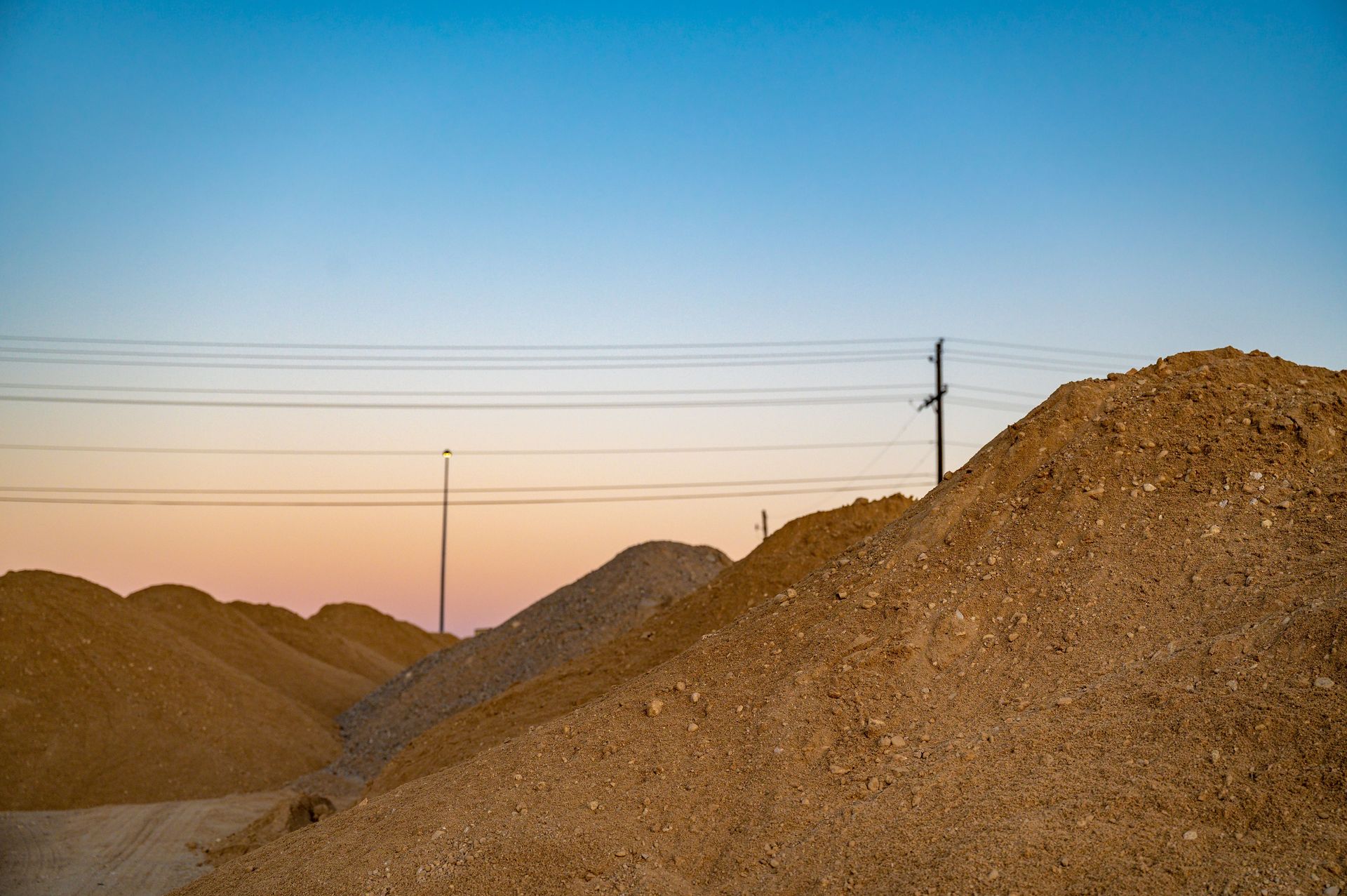 Large mounds of soil under a vibrant evening sky create a serene landscape with utility poles in the background.